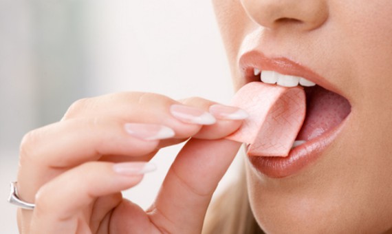 A female putting a piece of chewing gum in her mouth.
