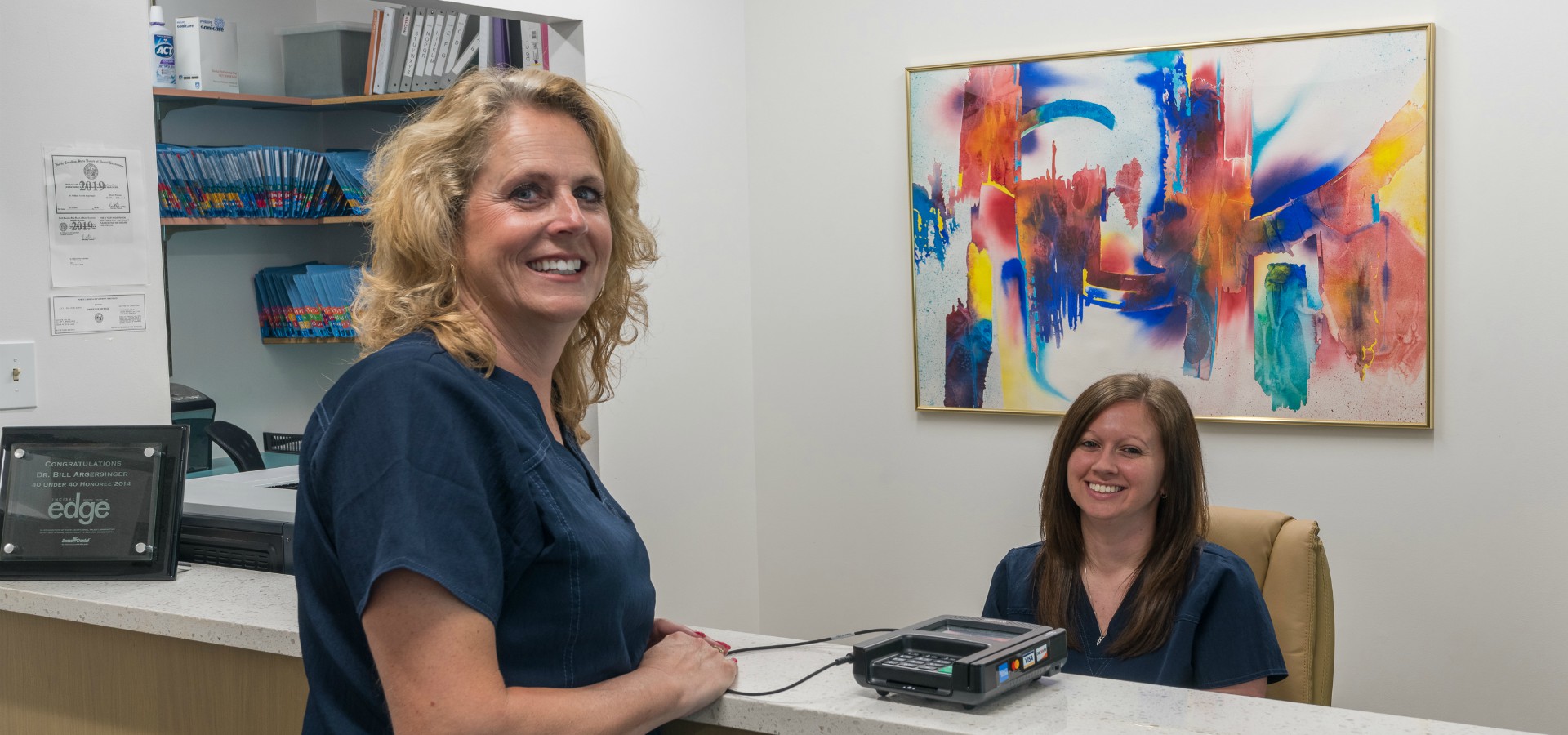 Two staff members at Durham DDS smiling in front of check out counter.