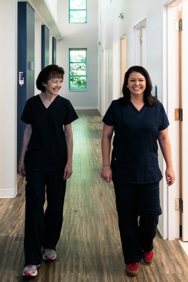 Two female employees of DurhamDDS walking down a hallway smiling.